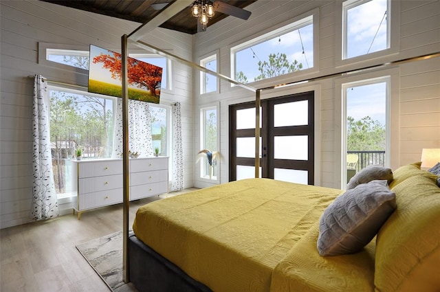 bedroom featuring access to exterior, wood walls, a towering ceiling, and wood finished floors