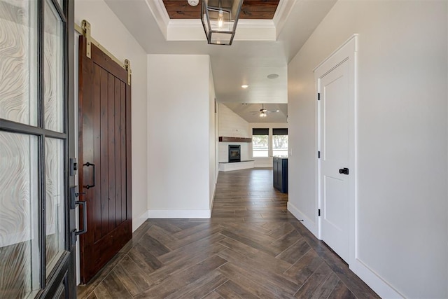 foyer with a ceiling fan, a glass covered fireplace, a barn door, crown molding, and baseboards