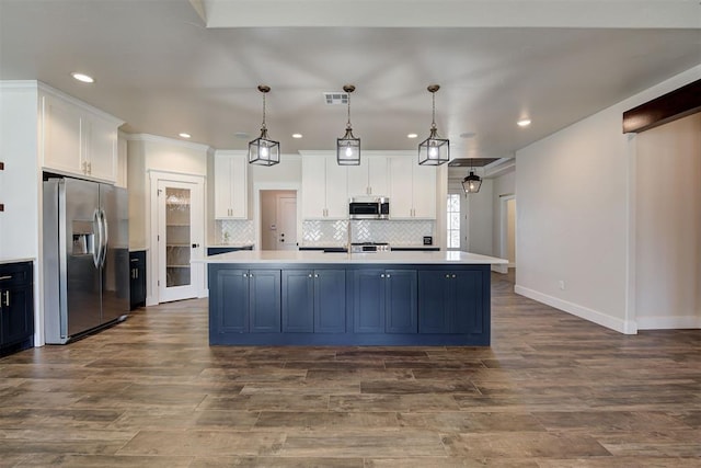 kitchen with backsplash, a center island with sink, light countertops, white cabinets, and stainless steel appliances