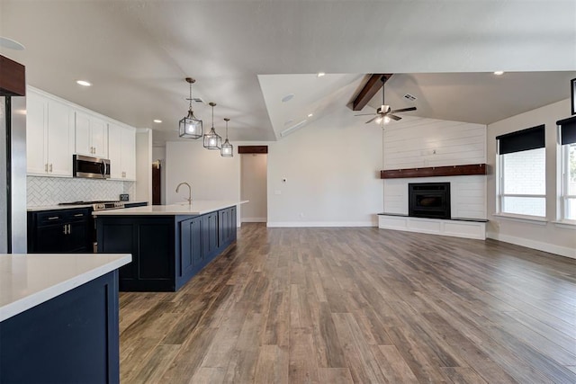 kitchen with stainless steel microwave, white cabinets, light countertops, ceiling fan, and vaulted ceiling with beams