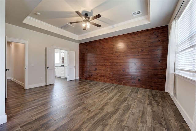 unfurnished bedroom featuring visible vents, dark wood-type flooring, ornamental molding, a tray ceiling, and wood walls