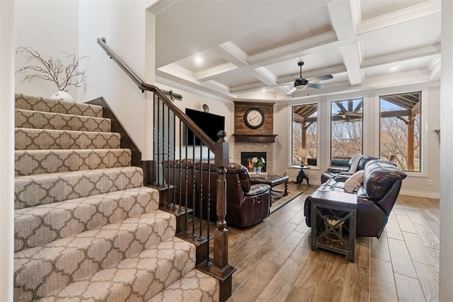 living area with ceiling fan, stairway, beamed ceiling, a fireplace, and wood finished floors