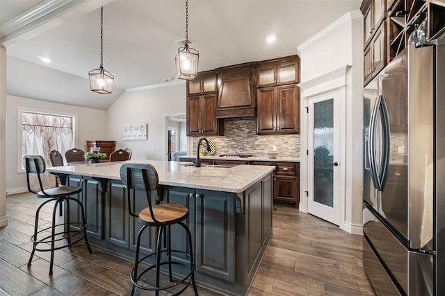 kitchen featuring tasteful backsplash, stainless steel fridge with ice dispenser, a breakfast bar area, custom exhaust hood, and a sink