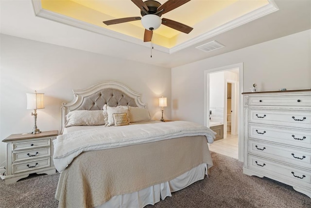 bedroom featuring visible vents, connected bathroom, a tray ceiling, ornamental molding, and carpet flooring