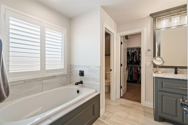 bathroom with vanity, a garden tub, a walk in closet, and toilet