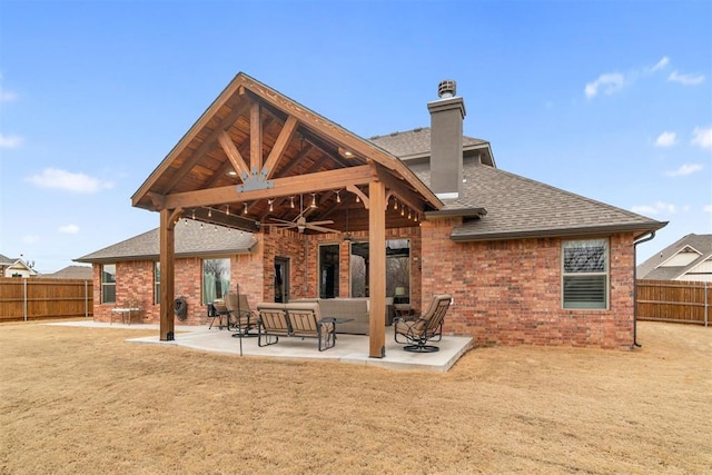 rear view of house featuring a ceiling fan, roof with shingles, a fenced backyard, a chimney, and brick siding