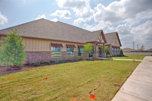 view of front facade featuring brick siding, board and batten siding, a front yard, and roof with shingles