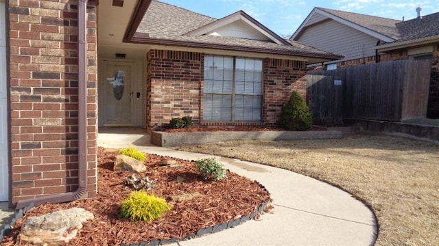 property entrance featuring brick siding, a shingled roof, and fence