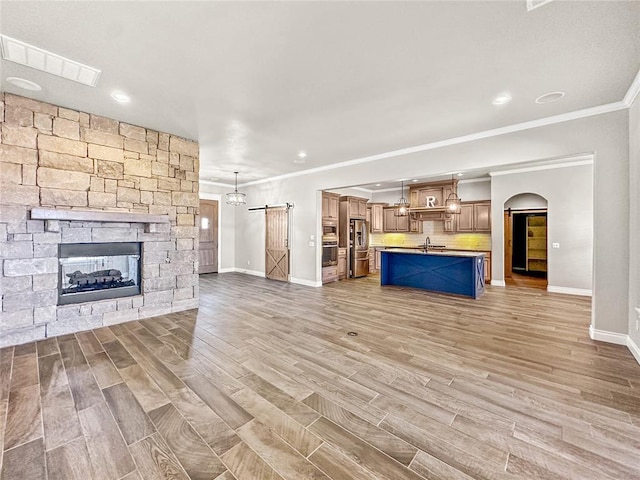 unfurnished living room with light wood-type flooring, visible vents, a sink, a barn door, and a fireplace