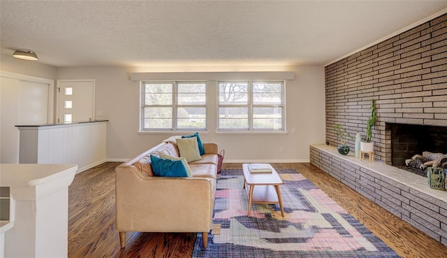 living area featuring a brick fireplace, wood finished floors, baseboards, and a textured ceiling