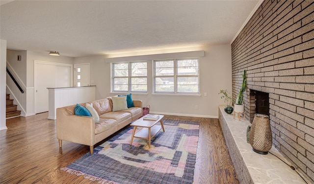 living area with a brick fireplace, wood finished floors, baseboards, and a textured ceiling