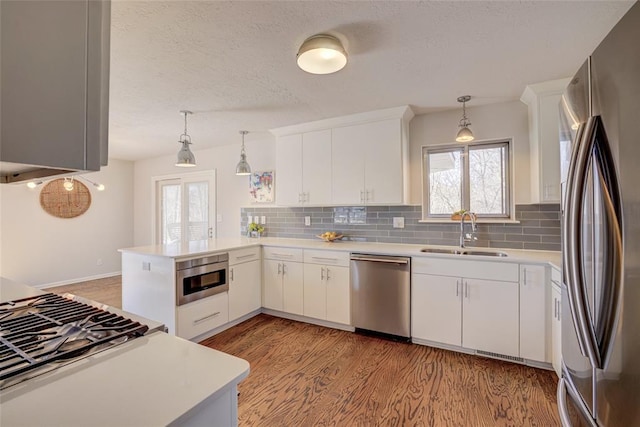 kitchen featuring light wood finished floors, a sink, appliances with stainless steel finishes, a peninsula, and light countertops