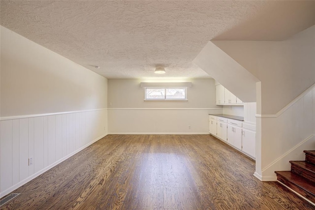 bonus room with visible vents, a wainscoted wall, a textured ceiling, wood finished floors, and stairs