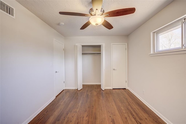 unfurnished bedroom featuring visible vents, ceiling fan, baseboards, wood finished floors, and a textured ceiling