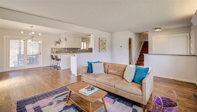living area featuring baseboards, an inviting chandelier, wood finished floors, and stairway