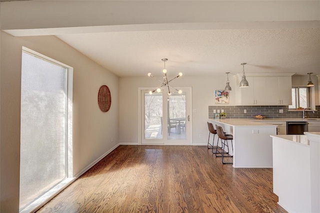 kitchen with light countertops, white cabinetry, wood finished floors, a kitchen bar, and dishwashing machine