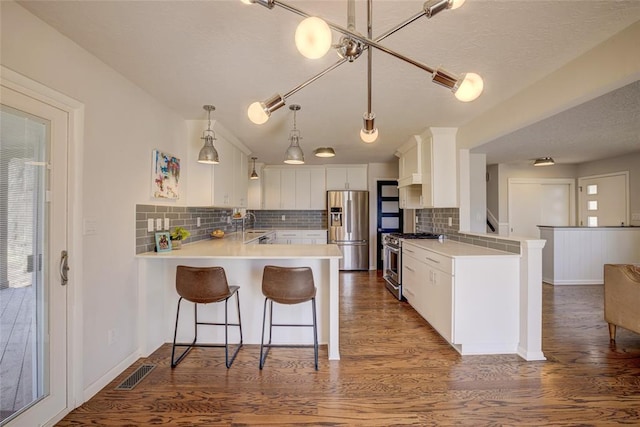 kitchen with light countertops, dark wood finished floors, stainless steel appliances, a peninsula, and backsplash