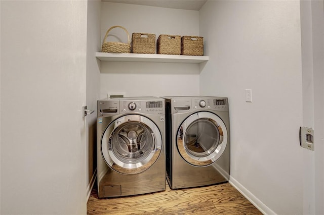clothes washing area with laundry area, baseboards, wood finished floors, and washer and dryer