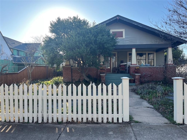 bungalow featuring a fenced front yard, covered porch, and brick siding