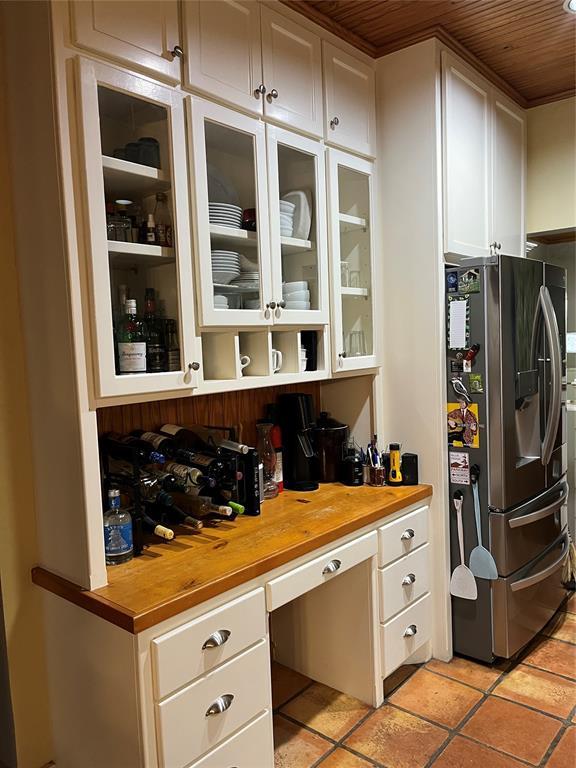 kitchen featuring butcher block countertops, light tile patterned flooring, stainless steel fridge with ice dispenser, white cabinets, and glass insert cabinets