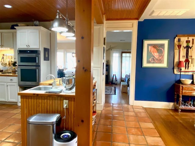 kitchen with visible vents, double oven, wood ceiling, white cabinetry, and a sink