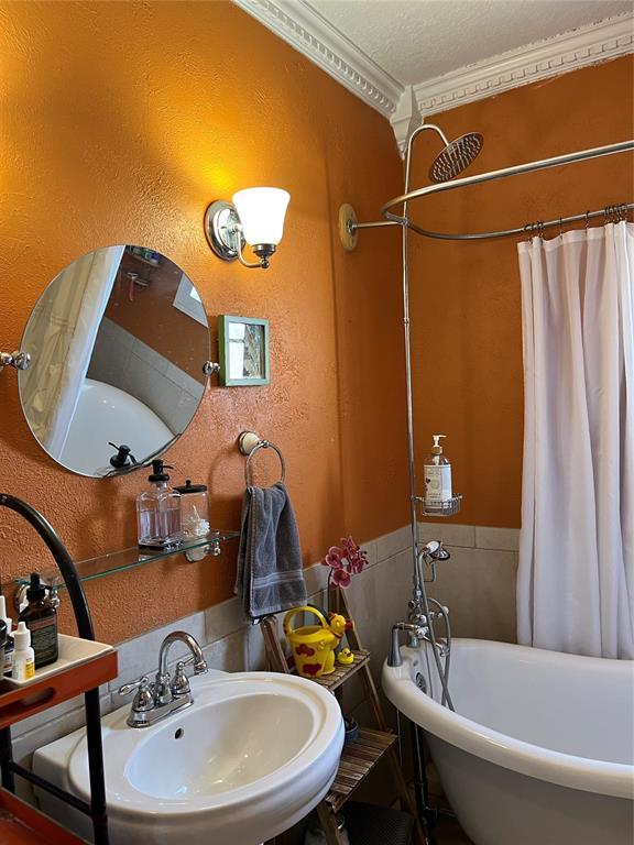 full bath featuring a washtub, crown molding, a textured wall, and a sink