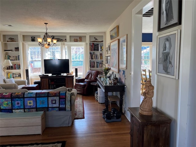 living area with built in shelves, wood finished floors, visible vents, an inviting chandelier, and a textured ceiling