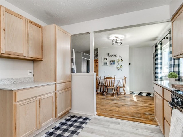 kitchen featuring light brown cabinets, a textured ceiling, range, light wood-style floors, and baseboards