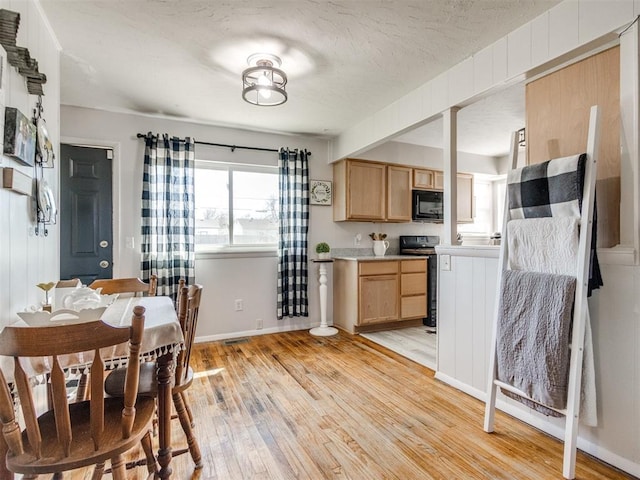 kitchen with light brown cabinets, light wood finished floors, stove, light countertops, and black microwave