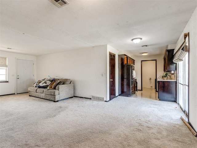 unfurnished living room with visible vents, light colored carpet, and a textured ceiling