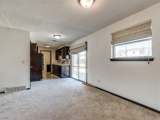 spare room with visible vents, plenty of natural light, light carpet, and a textured wall