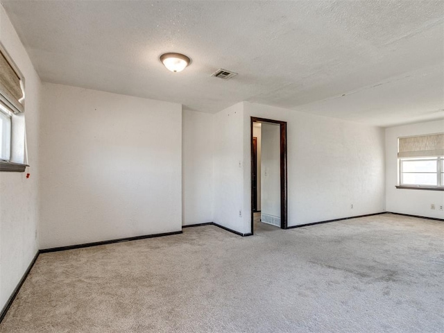 carpeted spare room with baseboards, visible vents, and a textured ceiling