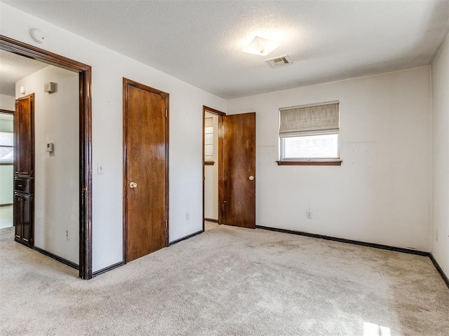 unfurnished bedroom with baseboards, light colored carpet, visible vents, and a textured ceiling