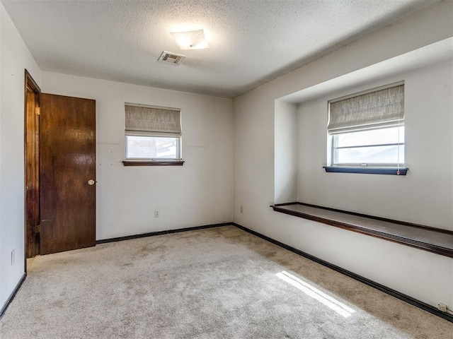 spare room featuring visible vents, plenty of natural light, carpet, and a textured ceiling