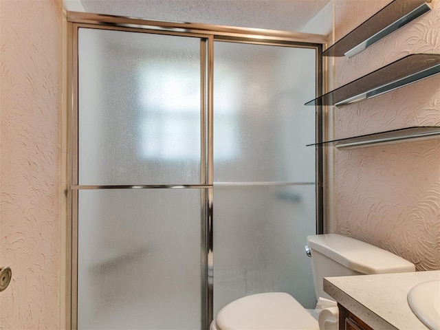 full bathroom featuring vanity, toilet, a textured wall, and a shower with shower door