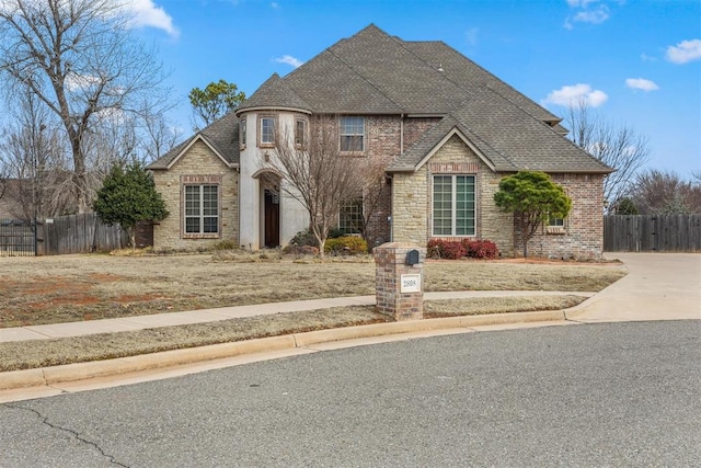 view of front of home with stone siding, brick siding, roof with shingles, and fence