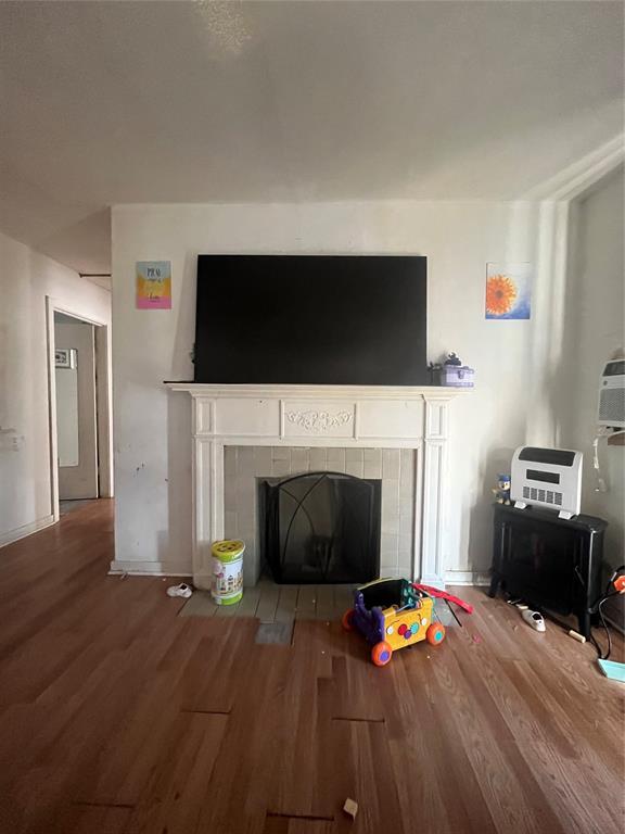 unfurnished living room featuring a tiled fireplace, baseboards, and wood finished floors