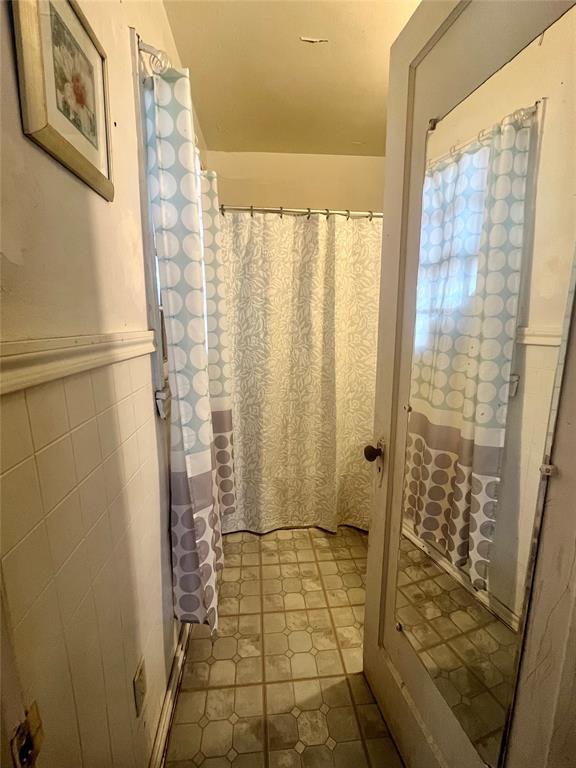 bathroom featuring wainscoting, tile walls, and a shower with curtain