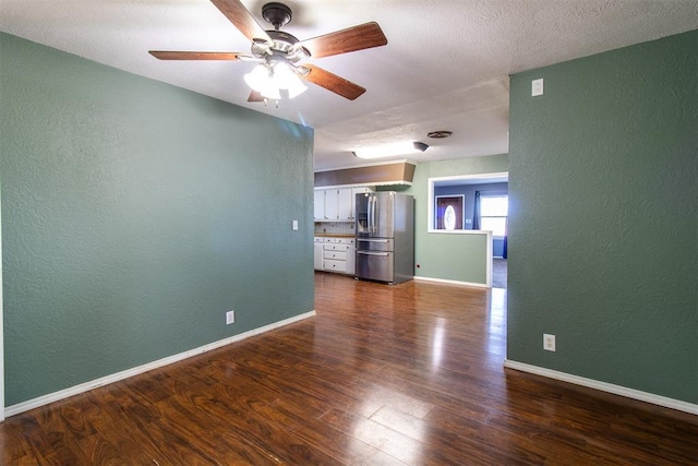 empty room with baseboards, dark wood-type flooring, a ceiling fan, and a textured wall