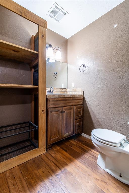 half bath with visible vents, toilet, wood-type flooring, vanity, and a textured wall