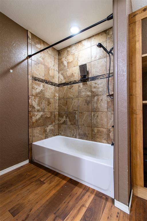 full bathroom featuring shower / washtub combination, wood finished floors, and a textured wall