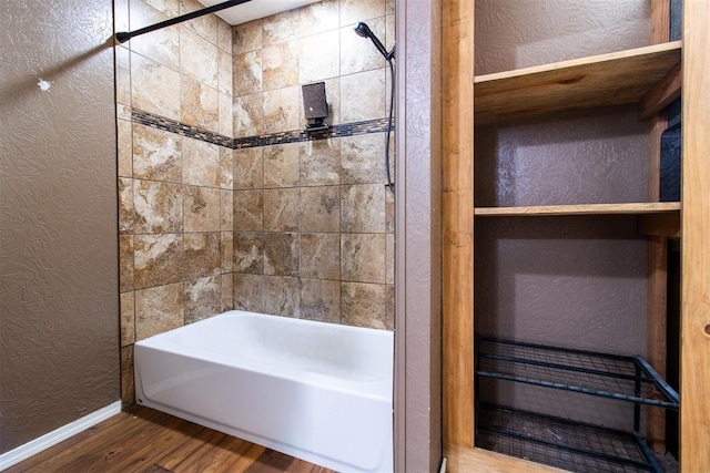 bathroom featuring wood finished floors, shower / tub combination, a textured wall, and baseboards