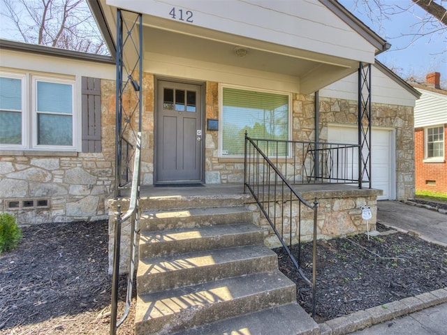 view of exterior entry featuring stone siding, an attached garage, covered porch, and driveway