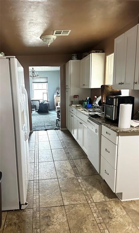 kitchen with white appliances, stone tile floors, and white cabinets