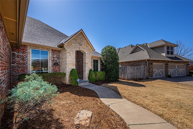 view of front of house featuring brick siding, roof with shingles, and fence