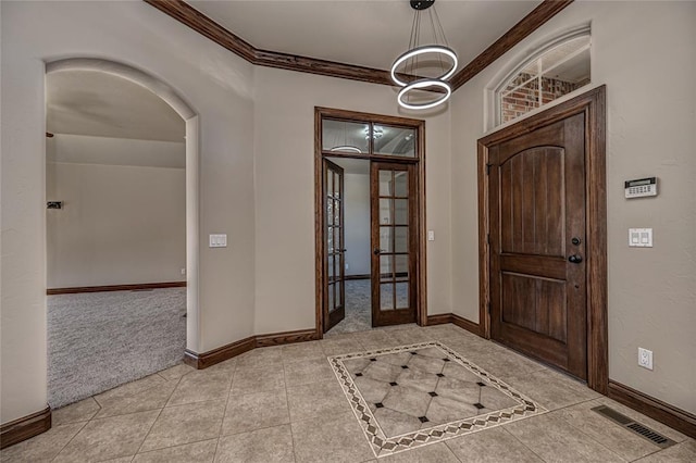 tiled foyer featuring arched walkways, baseboards, visible vents, and ornamental molding