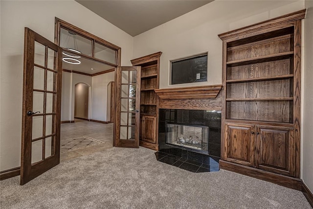 unfurnished living room with french doors, arched walkways, carpet, a fireplace, and baseboards