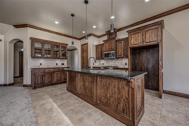 kitchen with tasteful backsplash, stainless steel microwave, glass insert cabinets, arched walkways, and a sink