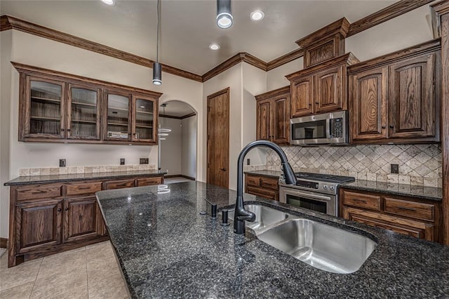 kitchen featuring backsplash, ornamental molding, appliances with stainless steel finishes, arched walkways, and a sink