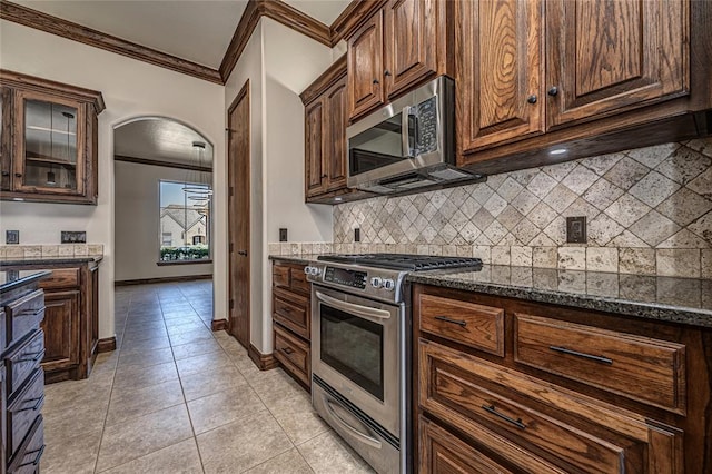 kitchen with backsplash, crown molding, light tile patterned flooring, arched walkways, and stainless steel appliances